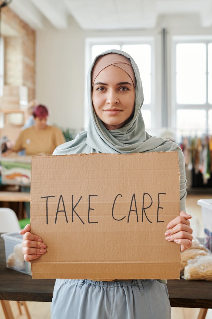 Crafting Captivating Headlines: Your awesome post title goes here Young woman in hijab proudly displaying a 'Take Care' sign indoors.
